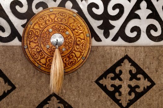 Antique national kazakh wall with shield, decoration in gold color on the background of a carpet with patterns.