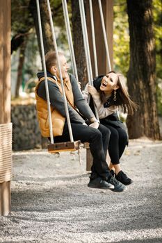 Happy cheerful couple close-up in autumn in the park in the forest in the afternoon on a wooden swing. High quality photo