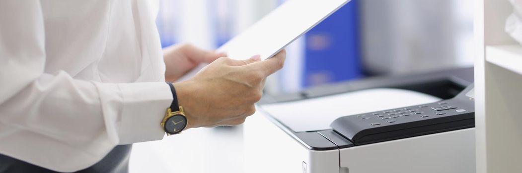 Close-up of female hands holding documents. Businesswoman standing near copier in office. Annual report and routine paper work concept. Business and management idea