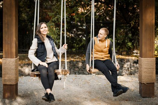 A young man with his lover are sitting on a swing in the forest among the trees. High quality photo