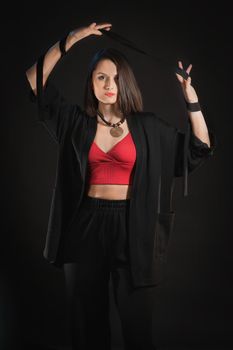 Fashion studio shot in low key with woman with belt in raised hands in black sleepwear.