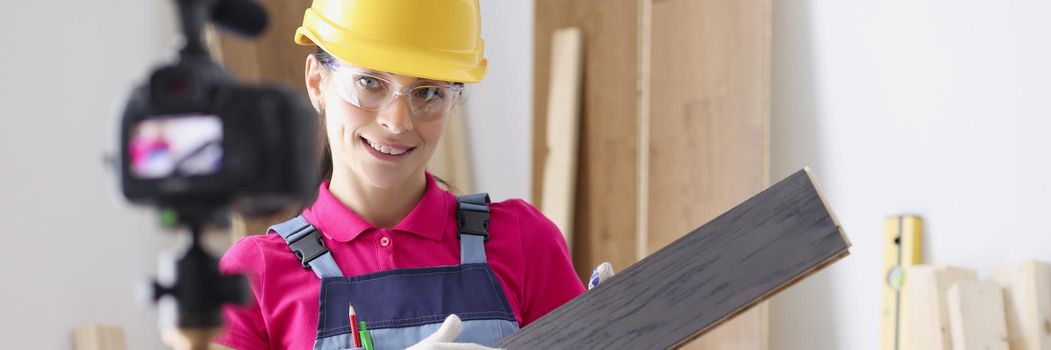 Portrait of professional female worker holding laminate board and showing to camera. Repairer perform construction task, renovation in home. Building blogging and vlogging idea. Redecoration concept