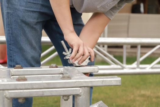 Close-up worker hands assemble a mobile stage from trusses for a outdoor concert.