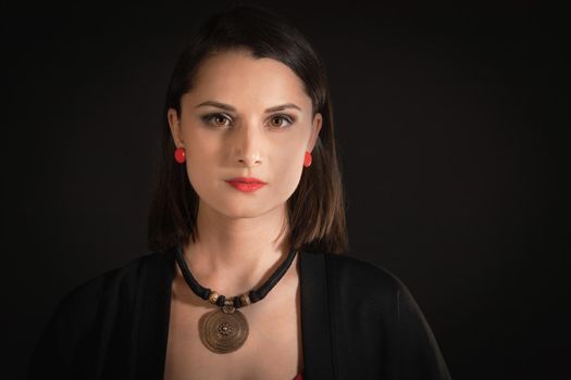 Portrait of 30s woman with oriental necklace on the neck of in boho style in black clothes.