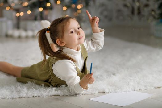 Good idea what to ask Santa Claus. Cute kid girl in christmas interior, finger up.