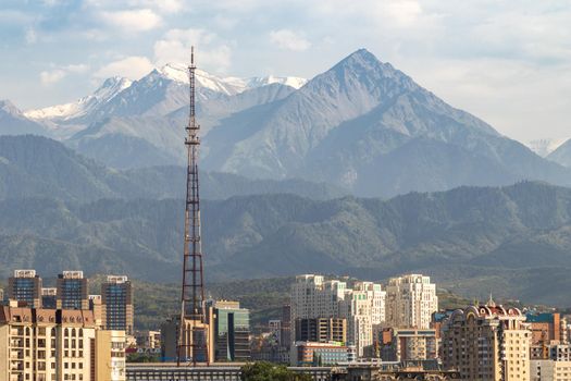 View of the city of Almaty with new residential complexes and an old radio and television tower against the backdrop of mountains. Almaty, Kazakhstan - July, 02, 2021
