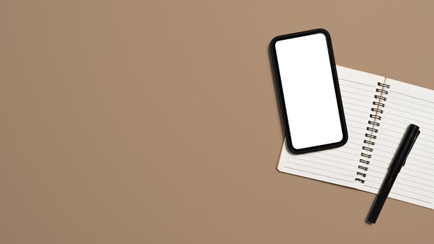Top view mobile phone with empty screen ad notebook on beige background. Copy space.