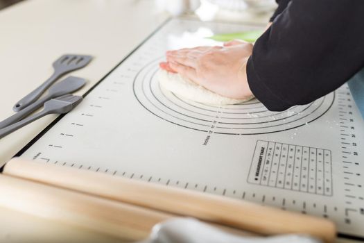 Side view of kneading dough on rubber kitchen mat on white kitchen table.