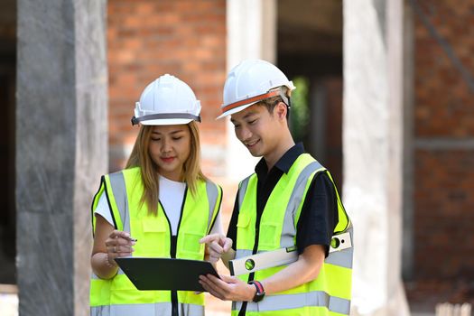 Two satisfied engineers wearing uniform and safety helmet inspecting industrial building construction site. Industry, Engineer, construction concept.