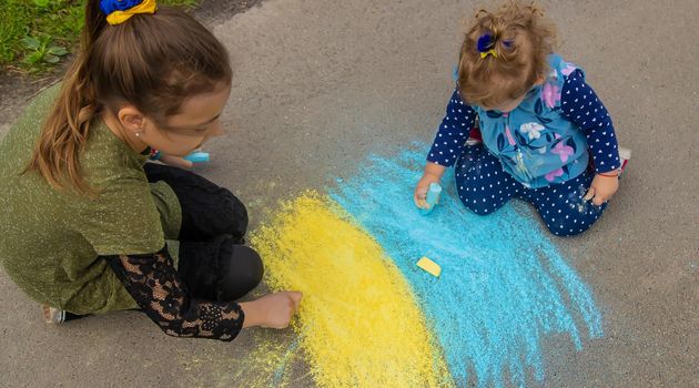 Children draw the Ukrainian flag on the pavement. Selective focus. Nature.