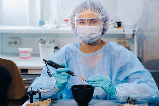 A dental technician in protective clothing is working on a prosthetic tooth in his laboratory.