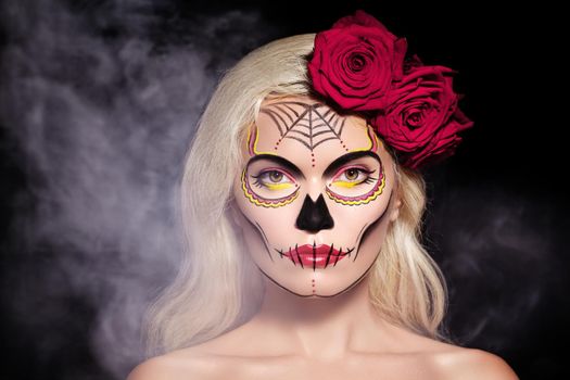 Beautiful Halloween Make-Up Style. Blond Model Wear Sugar Skull Makeup with Red Roses, pale Skin Tones and Waves Hair. Dia de los Muertos or Day of the Dead or Santa Muerte concept