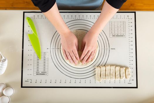 Top view of hands kneading rolled out dough on a kitchen baking mat with round markings of different diameters.