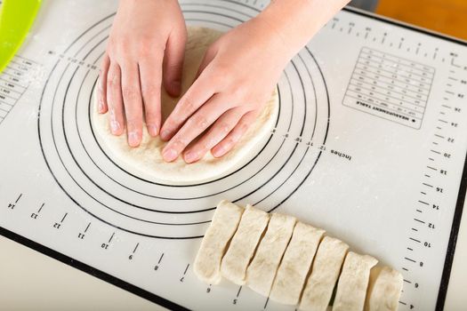 Close-up of hands kneading rolled out dough on a kitchen silicone mat with round markings of different diameters.