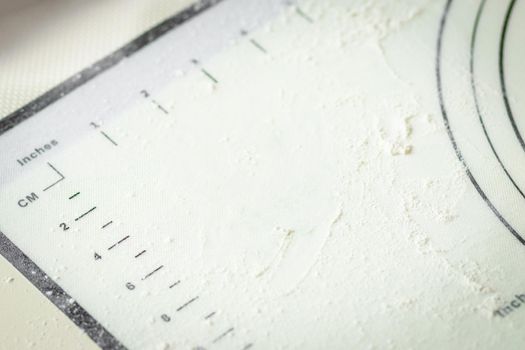 White silicone cooking mat with centimeter and inch markings sprinkled with flour, copy space.