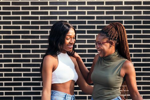 couple of young black girls laughing looking into each other's eyes with a brick wall in the background, concept of youth and friendship, copy space for text