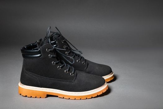 Pair of black winter men's suede boots on a gray background, side view and copy space.