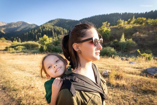 Babywearing woman with her daughter in ergonomic baby carrier travel in mountain.