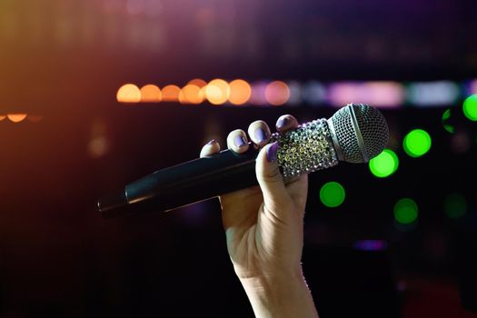 Woman hand holding wireless microphone with rhinestones on stage.