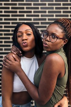 vertical portrait of two funny black friends throwing kisses at the camera, concept of youth and friendship, copy space for text