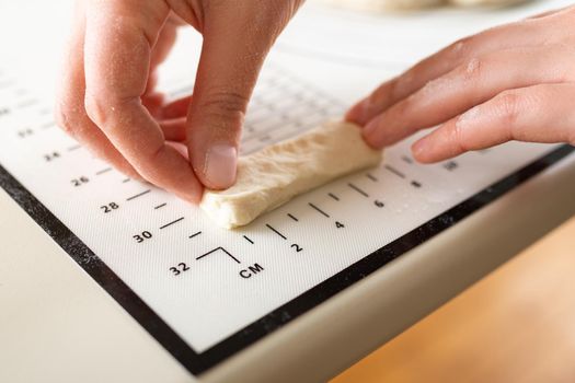 Close-up of the cook's hands measuring the length of a piece of dough on a silicone kitchen mat with markings.