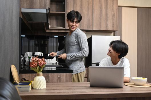 Young gay couple cooking in the kitchen together. Homosexual relationships and alternative love lifestyle concept.