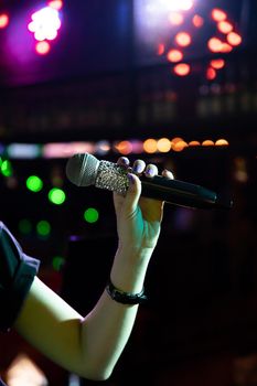 Microphone in female hand on stage in a dark nightclub.