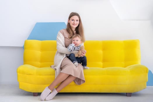 Portrait of a young european woman with a small child on a sofa in a bright positive interior.