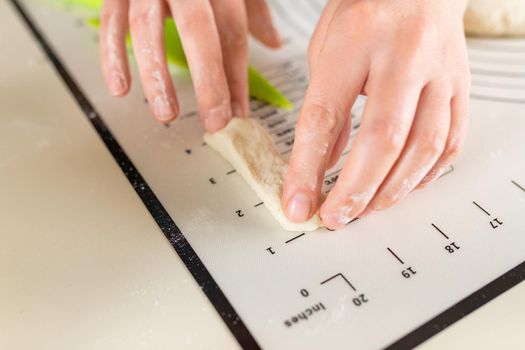 Close-up of hands measuring the length of a piece of dough on a kitchen mat with inch markings.