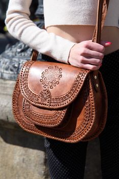 small brown women's leather bag with a carved pattern. street photo