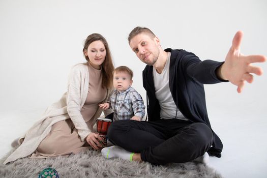Young caucasian parents with one year old son sit on carpet in white studio.