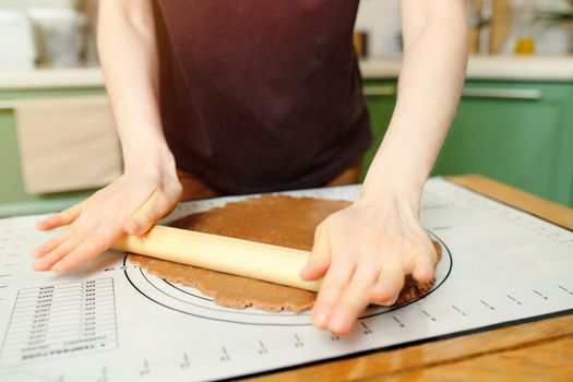 Rolling out brown dough for shortcrust bakery on a silicone baking mat on a wooden table.