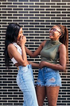 couple of young black girls laughing happy in front of a brick wall, concept of youth and friendship, copy space for text