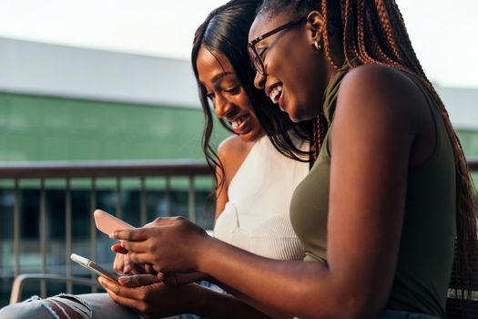two young black women laughing happily while consulting their mobile phones, concept of youth and communication, copy space for text
