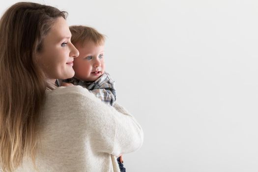 Young european mother with holds a baby in hugs on a white background, both look in one direction, copy space.