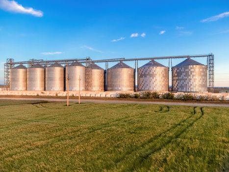 Grain elevator. Metal grain elevator in agricultural zone. Agriculture storage for harvest. Grain silos on green nature background. Exterior of agricultural factory