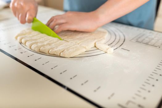 Side view on cutting wheat dough on a baking mat with markings with a plastic knife on the kitchen table, copy space.