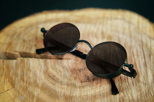 Black round sunglasses on a wooden stand. Fashionable unisex party accessory. Hippie or boho style.