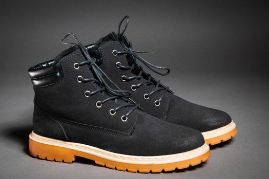 A pair of black winter men's boots with laces and a light sole on a gray background, side view.
