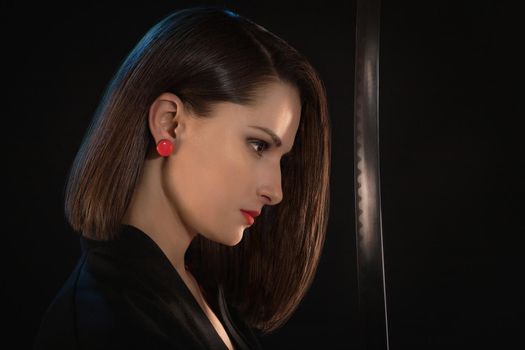 Portrait of a young woman with red lips and earrings in front of a sharp blade on a black background.