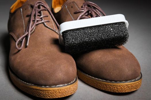 A black sponge for cleaning shoes lies on men's classic brown shoes with laces. Suede shoe care concept.