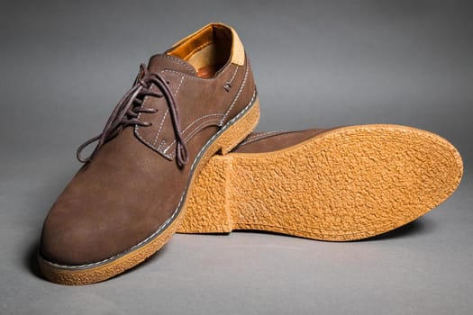 Brown suede modern shoes with laces on a grey background.