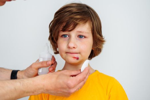 Dad doctor father treats bruised wound on his son school boy kid face. Man cleans addresses the sore wound on child face on white background with copy space for text.