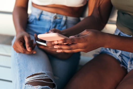 detail of the hands of an unrecognizable black woman showing her mobile phone to her friend, concept of youth and communication