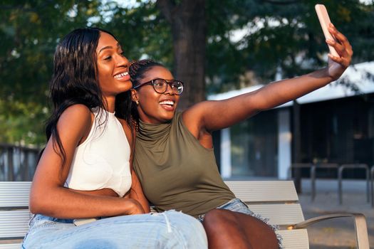 two young black women smiling happily while taking a selfie photo with the mobile phone, concept of fun and technology