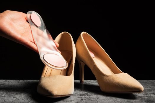 A woman's hand holds a soft orthopedic silicone insole in her hand next to a pair of classic high-heeled shoes.