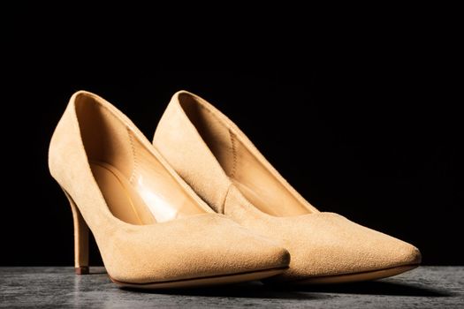 Cream-colored women's suede shoes with thin heels on a black background.