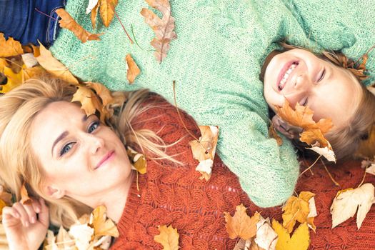 Little girl and young caucasian mom lying down directly above looking at camera on autumn leaves