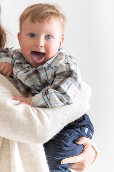 Portrait of a happy baby who shows his tongue in his mother's arms.