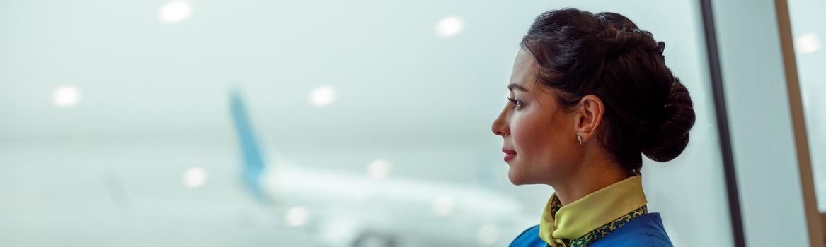 Woman stewardess in aviation air hostess uniform enjoying airfield view for window